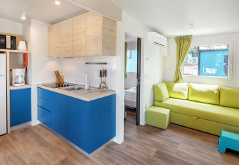 Moderne chalet Maro Home ved Valamar Camping Lanterna i Kroatien med blå køkken, grøn sofa og trægulv.