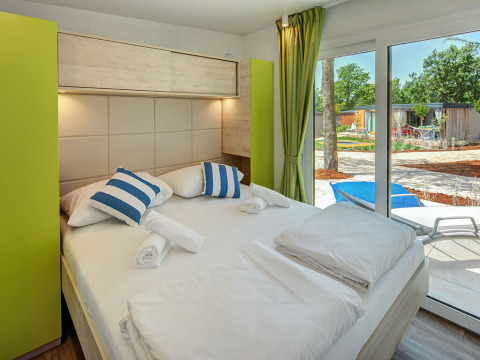 Modern bedroom inside Maro Home chalet at Valamar Camping Lanterna in Croatia, featuring terrace and garden view.