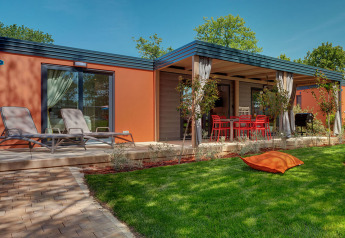 Maro Home chalet med orange vægge, liggestole, overdækket terrasse og grøn have under en klar himmel.