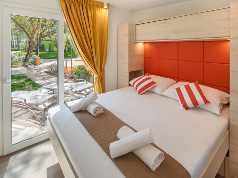Chalet moderne avec lit double, coussins rouges et terrasse chez Maro Home, Valamar Camping Lanterna, Croatie.