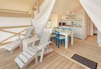 Heldere safaritent met houten terras, ligstoelen, eettafel en keuken bij Lanterna in Kroatië.