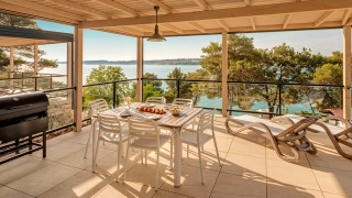 Große Terrasse der Marbello Suite mit Meerblick, Esstisch, Liegestühlen und Grill unter Dach.