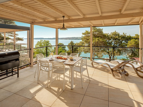 Grande terrasse à la Marbello Suite avec vue sur la mer, table à manger, transats et barbecue couvert.
