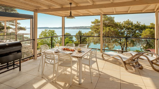 Große Terrasse der Marbello Suite mit Meerblick, Esstisch, Liegestühlen und Grill unter Dach.