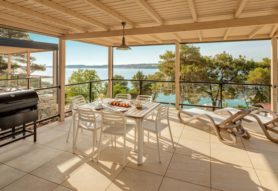 Grande terrasse à la Marbello Suite avec vue sur la mer, table à manger, transats et barbecue couvert.