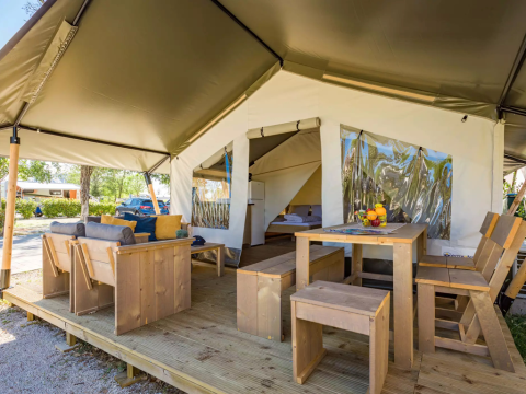 Safari-Zelt mit Holzmöbeln, gemütlichem Sitzbereich und Esstisch auf einer Holzterrasse im Freien.