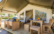 Tenda safari con mobili in legno, area soggiorno e pranzo esterna in un ambiente da campeggio rilassante.