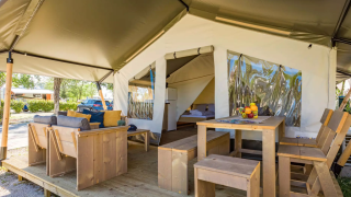 Safari-Zelt mit Holzmöbeln, gemütlichem Sitzbereich und Esstisch auf einer Holzterrasse im Freien.