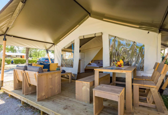 Tienda safari con muebles de madera, zonas exteriores para sentarse y comer en un entorno de camping.