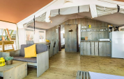 Interno di una spaziosa tenda safari con mobili in legno, angolo cottura, zona pranzo e salotto accogliente.