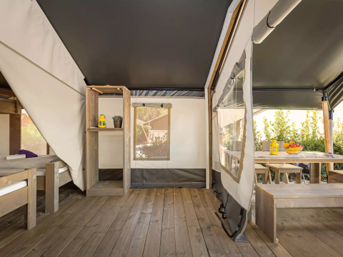 Interior de una tienda safari moderna con suelo de madera, camas y área de comedor exterior con fruta fresca.