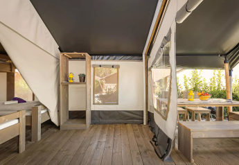 Interno di una moderna tenda safari con pavimento in legno, letti e zona pranzo esterna con frutta fresca.