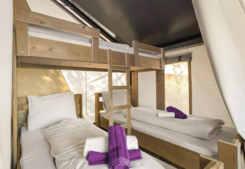 Interno di una tenda safari con letti a castello, due letti singoli, lenzuola bianche e asciugamani viola.