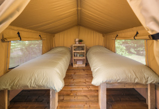 Vista interior de una tienda safari con dos camas individuales y suelo de madera en Holiday Park Mölke, Países Bajos.