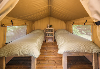 Vista interior de una tienda safari con dos camas individuales y suelo de madera en Holiday Park Mölke, Países Bajos.