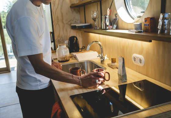 Uomo prepara il caffè in cucina moderna al Wrap house con sauna e vasca da bagno presso Resort de Parel, Paesi Bassi.