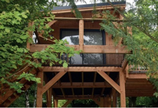 Boomhut aan Hameau de l'Ourthe in België, houten structuur tussen weelderige bomen, omgeven door groen.