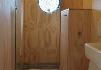 Bagno compatto con pareti in legno, finestra rotonda e WC al Wrap house nel Resort de Parel, Paesi Bassi.