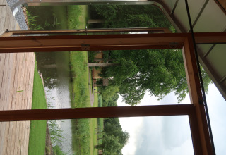 Vista dalla Wrap House al Resort de Parel nei Paesi Bassi, con terrazza in legno, stagno e alberi verdi.