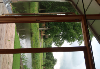 Vista dalla Wrap House al Resort de Parel nei Paesi Bassi, con terrazza in legno, stagno e alberi verdi.