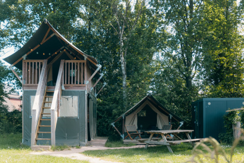 Safarihuisje XS met eigen sanitair bij Holiday Park Sallandshoeve, tussen bomen en veel groen.