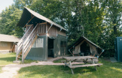 Tienda safari de dos pisos con terraza y pequeña tienda extra en Holiday Park Sallandshoeve, rodeado de árboles.