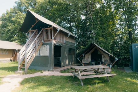Tente safari à deux étages avec terrasse et petite tente annexe au Holiday Park Sallandshoeve, entouré d'arbres.