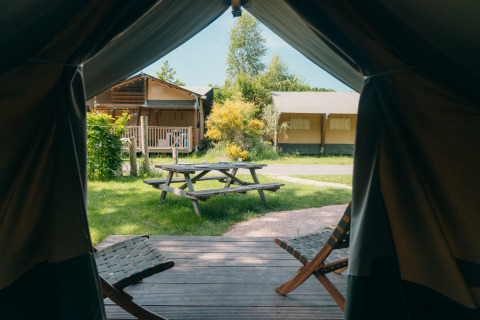 Vista desde el interior de una tienda safari a una mesa de pícnic y cabañas en Holiday Park Sallandshoeve, Países Bajos.