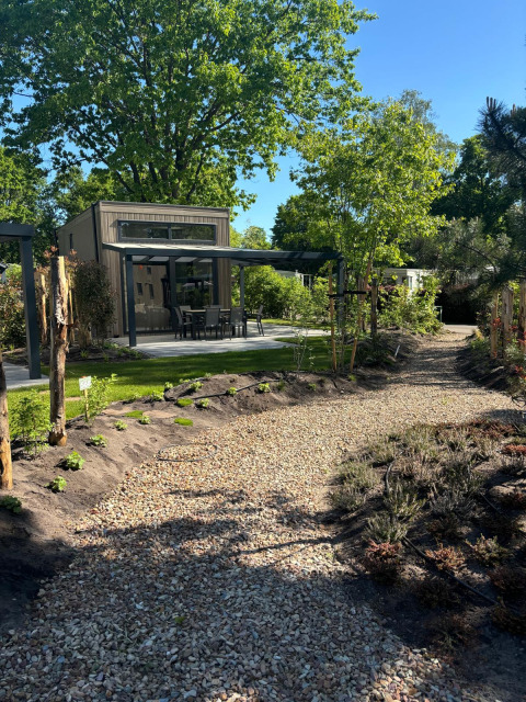 Kiesweg führt zur Reeëndal Lodge mit moderner Terrasse, umgeben von grünen Bäumen und Büschen.