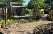 Grindpad leidt naar Reeëndal Lodge met modern terras en omringd door groene bomen en planten.