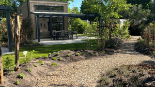 Kiesweg führt zur Reeëndal Lodge mit moderner Terrasse, umgeben von grünen Bäumen und Büschen.