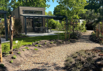 Gravel path leading to Reeëndal Lodge, featuring a patio with chairs, surrounded by lush greenery and trees.