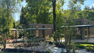 Zonnige dag bij Reeëndal Lodge in Veluwepark de Bosgraaf, Nederland, omringd door groene bomen.