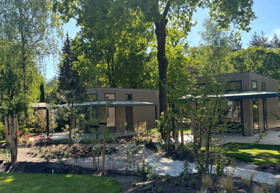 Zonnige dag bij Reeëndal Lodge in Veluwepark de Bosgraaf, Nederland, omringd door groene bomen.