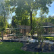 Sunny day at Reeëndal Lodge in Veluwepark de Bosgraaf, Netherlands, with lush greenery and modern lodges.