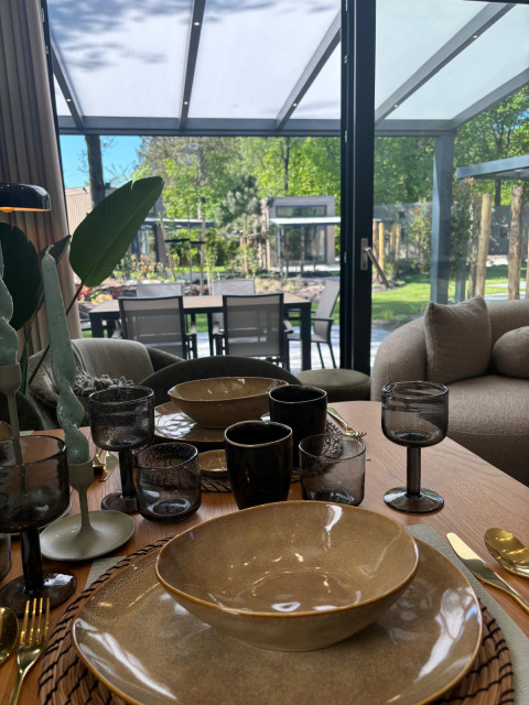 Set dining table at Reeëndal Lodge, Veluwepark de Bosgraaf, Netherlands, with view to patio and garden.