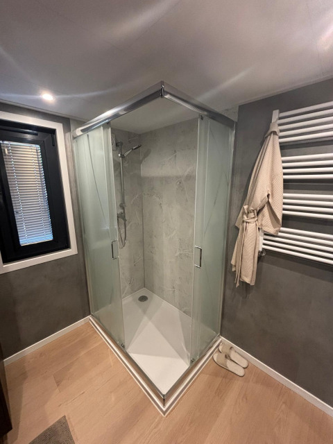 Bagno moderno con doccia triangolare in vetro, porta asciugamani e pavimento in legno al Reeëndal Lodge, Veluwepark de Bosgraaf.