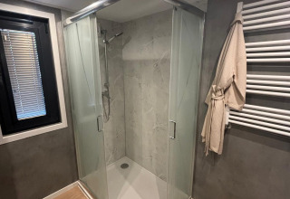 Baño moderno con ducha triangular de cristal, toallero y suelo de madera en Reeëndal Lodge, Veluwepark de Bosgraaf.
