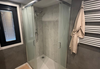 Baño moderno con ducha triangular de cristal, toallero y suelo de madera en Reeëndal Lodge, Veluwepark de Bosgraaf.