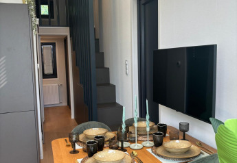 Modern dining space with four green chairs, wood table, and wall TV at Reeëndal Lodge, Veluwepark de Bosgraaf.