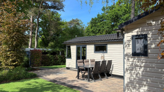 Außenbereich des Veluwe Chalet mit Garten, Sitzgruppe und Bäumen bei sonnigem Wetter.