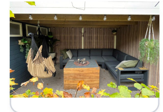 Hyggelig udendørs opholdsstue med hjørnesofa, hængekøje og bålplads i Veluwe Chalet, Veluwepark de Bosgraaf.