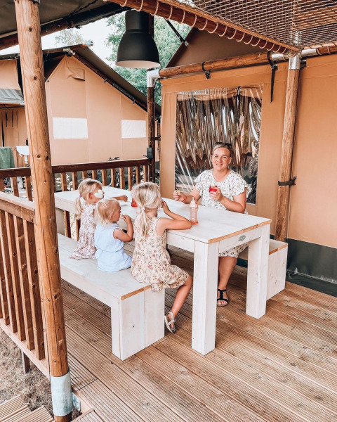Familia sentada en mesa frente a tienda Ranger Lodge en Holiday Park Sallandshoeve, Países Bajos.
