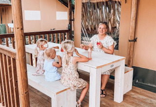 Famiglia seduta a tavola davanti a una tenda Ranger Lodge a Holiday Park Sallandshoeve, Paesi Bassi.