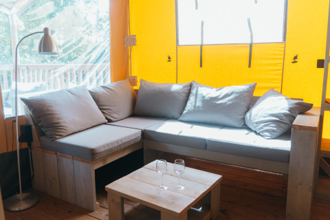 Bright lounge inside a Ranger Lodge safari tent at Holiday Park Sallandshoeve, Netherlands, with sofa and table.