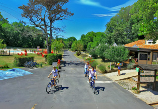 Familier cykler på vejene i Camping Le Périgord feriepark, omgivet af natur og faciliteter i Frankrig.