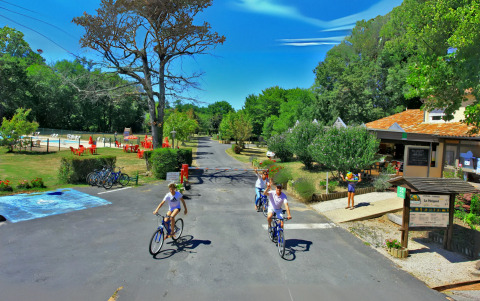Familier cykler på vejene i Camping Le Périgord feriepark, omgivet af natur og faciliteter i Frankrig.