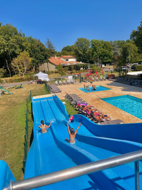 Bambini si divertono sugli scivoli blu accanto alla piscina del Camping Le Périgord in Nouvelle-Aquitaine, Francia.