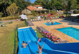 Bambini si divertono sugli scivoli blu accanto alla piscina del Camping Le Périgord in Nouvelle-Aquitaine, Francia.