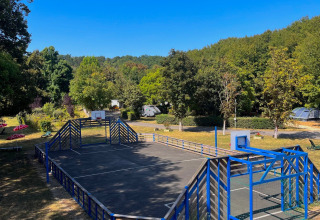 Sports court with blue fencing at Camping Le Périgord in Nouvelle-Aquitaine, France, surrounded by greenery.